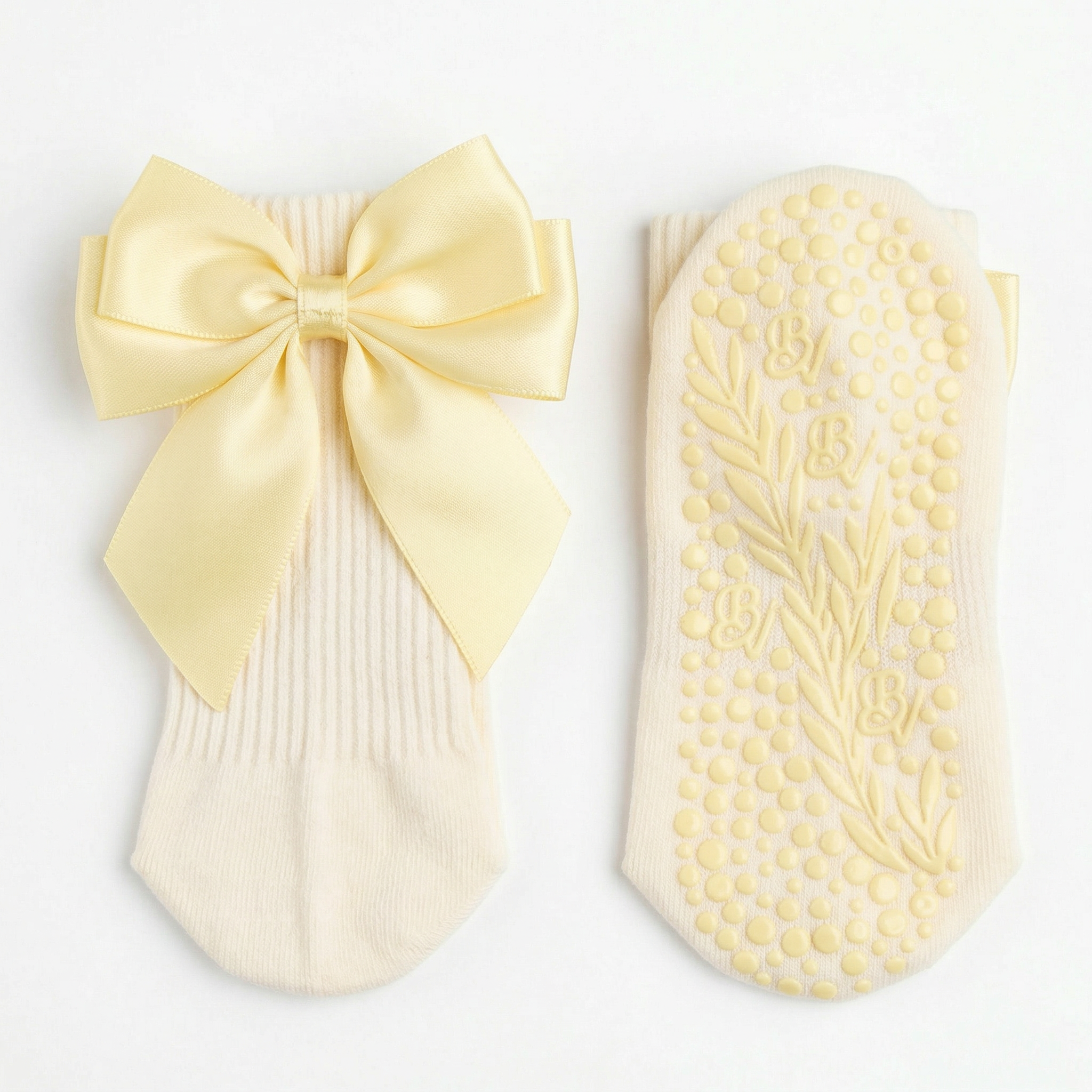 The Signature Ribbon Pilates Socks – Organic Cotton in Banana Yellow: one sock features a vintage-inspired satin bow at the back, while the other displays a high-traction sole with decorative leaf patterns.
