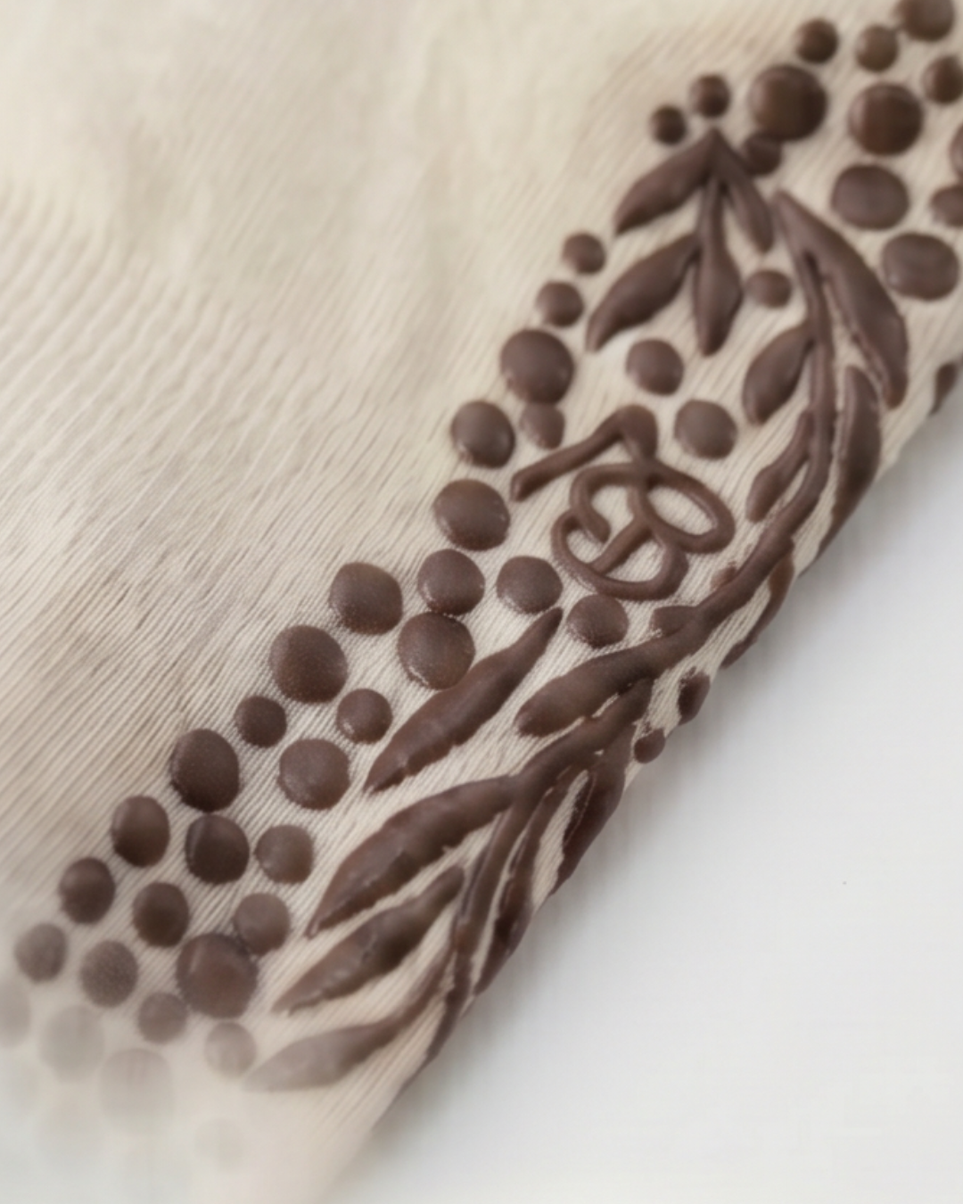 A close-up of The Minimalist Grip Crew – Organic Cotton - Brown, featuring light fabric with raised brown patterns—dots, leaves, and a central intertwined circular symbol.