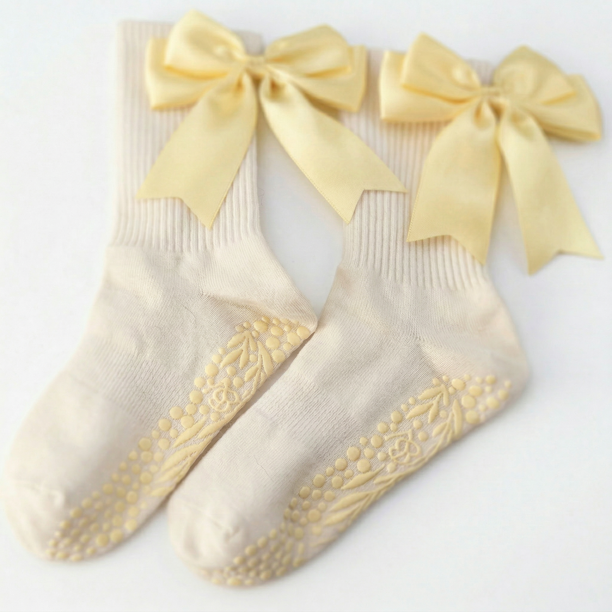 A pair of The Signature Ribbon Pilates Socks in banana yellow organic cotton, featuring large vintage satin bows and non-slip floral grip soles, laid side by side on a white background.