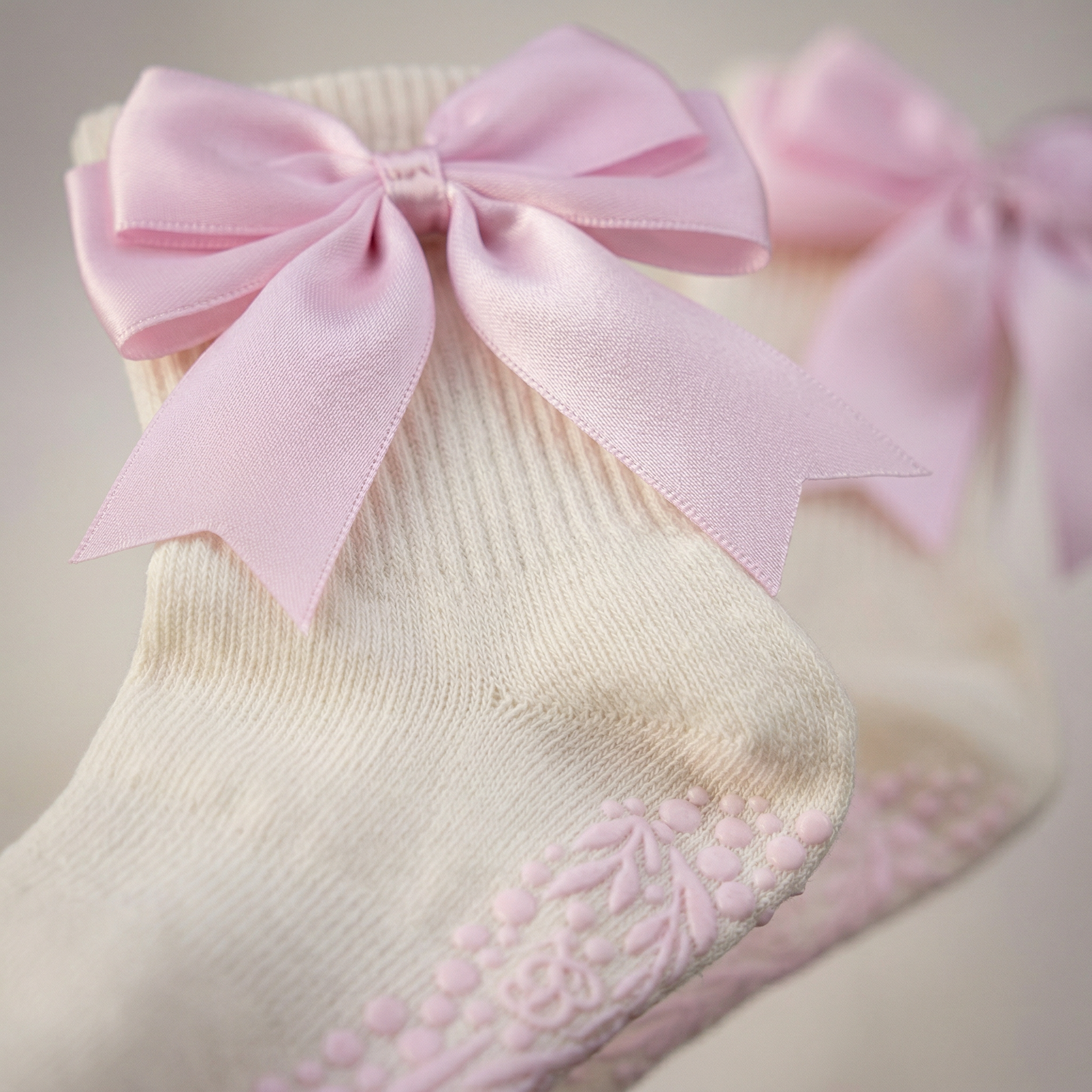 Close-up of The Signature Ribbon Pilates Socks – Organic Cotton - Rosehip Blush, featuring cream-colored fabric, a vintage-style satin bow, and pink rubber floral grip patterns for traction on the soles.